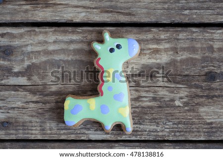 Homemade gingerbread cookie in the shape of green giraffe in purple and yellow spots on a wooden background. Space for text and selective focus.
