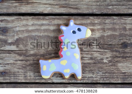 Homemade gingerbread cookie in the shape of violet giraffe in green and yellow spots on a wooden background. Space for text and selective focus.