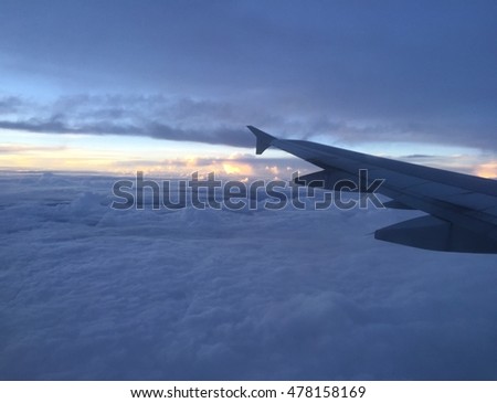 Flying high with the beautiful clouds. The sun setting behind clouds getting ready to rumble with a storm. Perfect view from the window of an airplane. Right behind the left wing.  Royalty-Free Stock Photo #478158169