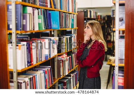 Pensive girl chosing a book in college library. Education concept