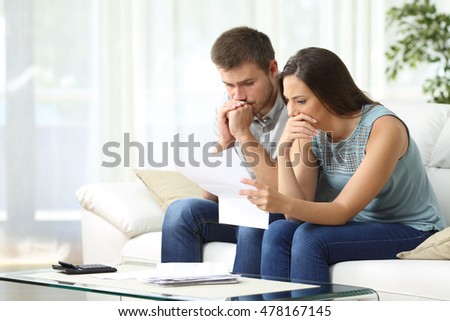 Worried couple reading an important notification in a letter sitting on a couch in the living room at home Royalty-Free Stock Photo #478167145