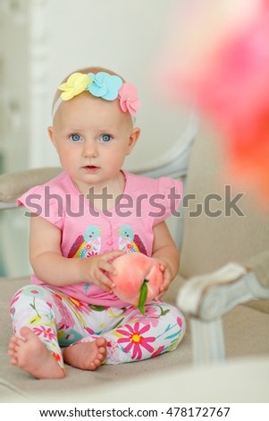 Little beautiful baby girl with big blue eyes, sitting on a chair with a peach in his hand