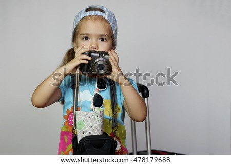 Cute little girl in casual standing with travel suitcase and camera bag holding paper map and going on a journey over white background, family vacation concept