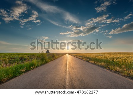 Driving on an empty asphalt road through the wheat and soybean fields towards the setting sun. Royalty-Free Stock Photo #478182277