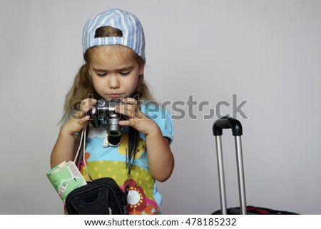 Cute little girl in casual standing with travel suitcase and camera bag holding paper map and going on a journey over white background, family vacation concept