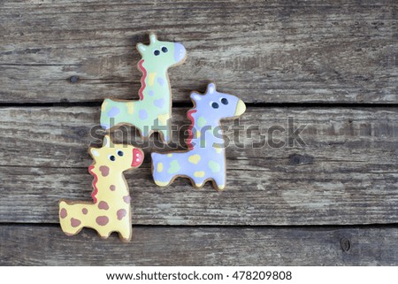 Homemade gingerbread cookie in the shape of violet, green and yellow giraffes on a wooden background. Space for text and selective focus.