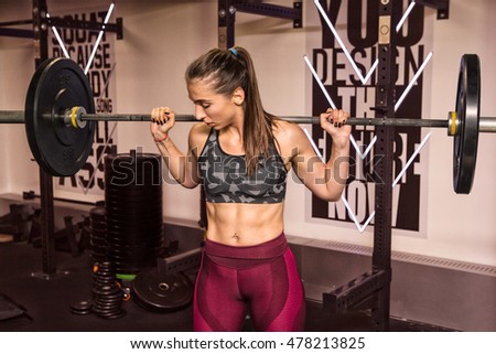 Young and beautiful woman with barbell on her shoulders