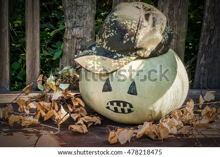 Funny pumpkin with a painted face in a hat on the old garden table with dried birch branches. Tinted photo