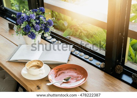 Empty coffee cup and empty plate after drink coffee and cake with book on wooden desk.