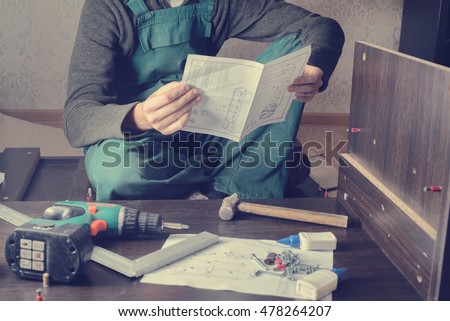 Frustrated man reading instruction and putting together self assembly furniture. DIY, new home and moving concept Royalty-Free Stock Photo #478264207