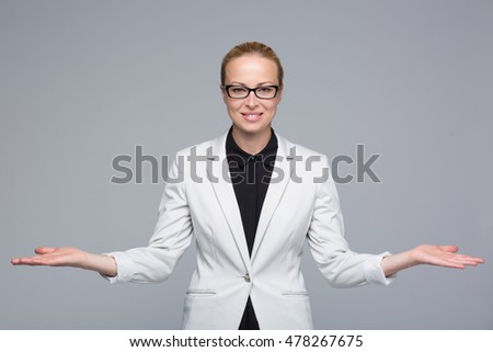 Beautiful young businesswoman smiling, holding open palms with empty copy space. Business woman showing hands sign to sides, concept of advertisement or comparing products. Grey background.