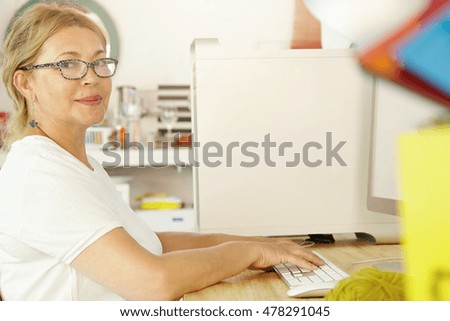 Profile picture of good-looking female pensioner in glassses changing activities while resting at home, using PC, browsing latest news, checking weather online, looking at camera with pleased smile