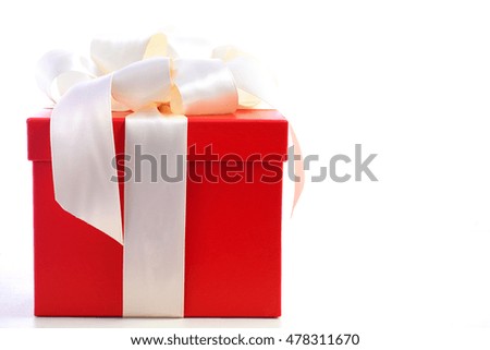 Bright red festive holiday gift box beautifully wrapped in cream white satin ribbon, on white wood table 