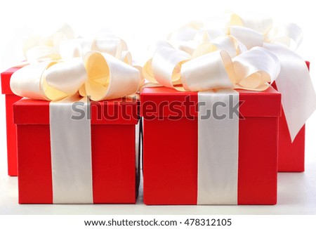 Bright red festive holiday gift boxes beautifully wrapped in cream white satin ribbon, on white wood table 