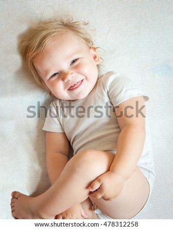  beautiful baby girl laying in white sunny bedroom. Newborn child relaxing on a rug. Nursery for young children. Furniture, textile and bedding for kids.