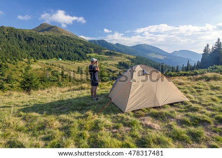 Photographer hiker standing near tent  taking pictures of mountains