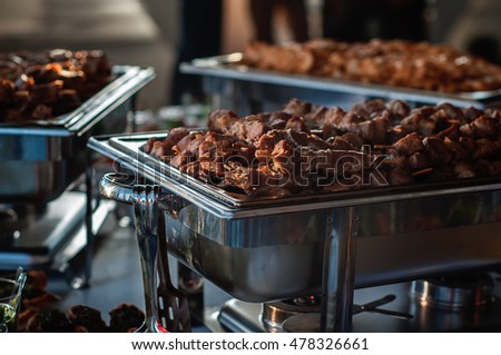 Buffet table. Mini marinated beef kabobs in metal stock pot, illuminated by the setting sun from the window. Photo in dark light style 