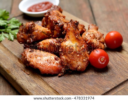 Fried chicken wings on rustic serving board, spicy tomato sauce, herbs and mug of light beer over black wooden backdrop, top view Royalty-Free Stock Photo #478331974