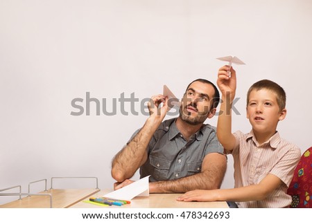 father teaches his son to do paper airplanes indoor