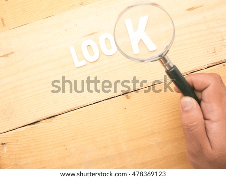 a hand holding a magnifying glass over a wooden background and alphabet with the word look