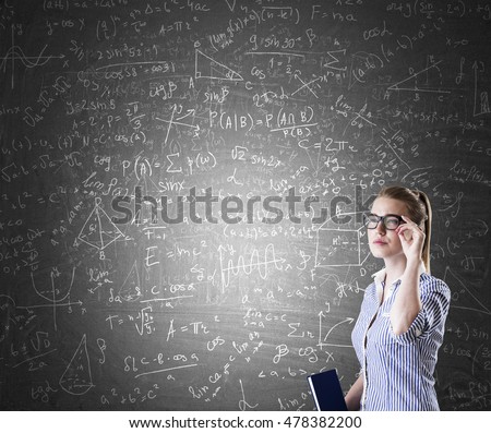 Nerd girl standing near blackboard with formulas and figures. Concept of engineering and exact sciences.