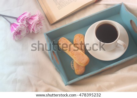 Dreamy image of romantic breakfast in the bed: cookies, hot coffee, flowers and open book. Vintage filtered