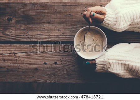 Woman holding cup of hot coffee on rustic wooden table, closeup photo of hands in warm sweater with mug, winter morning concept, top view Royalty-Free Stock Photo #478413721