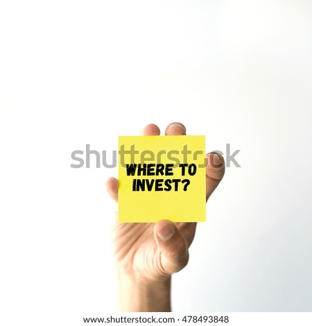Hand holding yellow sticky note written WHERE TO INVEST word