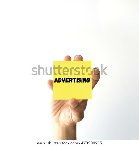 Hand holding yellow sticky note written ADVERTISING word