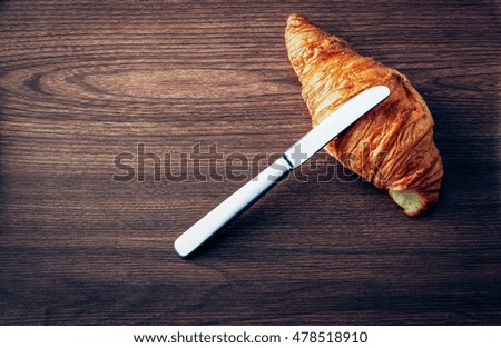 Croissant and knife on wooden table