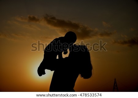 silhouette of a happy young mother,   playing with her toddler child at sunset