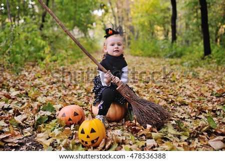 a little girl dressed as a witch on a broomstick on the background of autumn forest celebrates Halloween