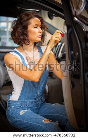 pretty mechanic woman in a blue overalls repair with a screwdriver the door of car