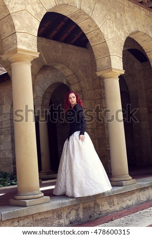 
beautiful red haired woman wearing a black and white gown, wandering around a castle.
