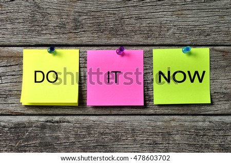 DO IT NOW text written on sticky note on wooden background. Motivational quotes
