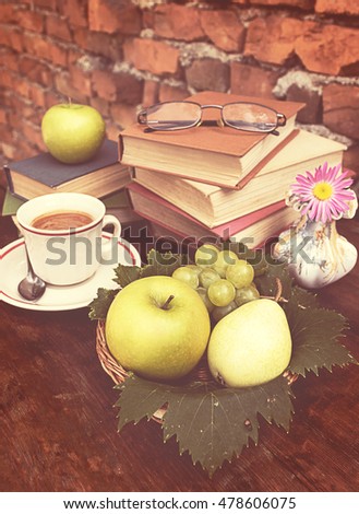 Composition with cup of fresh tasty coffee on a wooden table, vintage books, fresh fruits and vase with pink flower. Romantic morning theme with retro decor elements. Old brick wall background