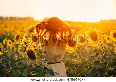 young redheaded woman in a field of sunflowers is back. the flowing hair, the sunset light