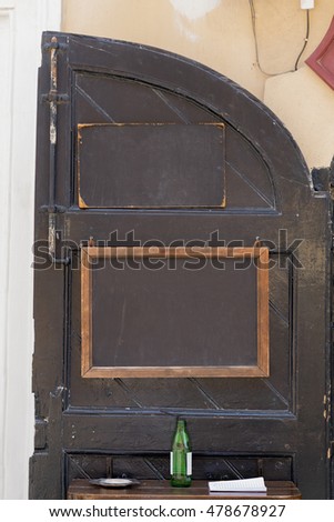 Black door with two clean black chalk boards and bottle of beer