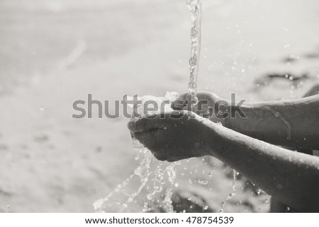 Black and white closeup on hands holding water, sunny day beach outdoors background