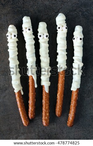 Group of Halloween mummy, candy dipped pretzel rods on black stone background