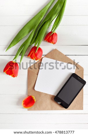 Spring bouquet of red tulips and black mobile phone on a white wooden background with copy space. View from the top with space for signature.