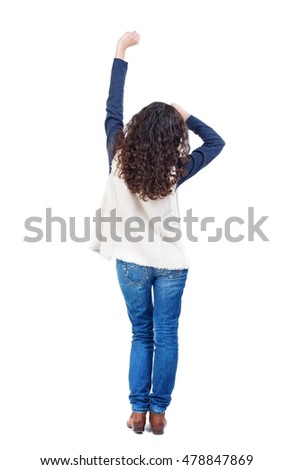 back view of dancing young beautiful woman. Long-haired girl with curly hair happily raised her hand with his fist.