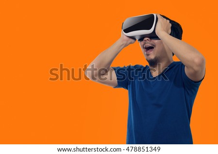 Young man with a virtual reality headset stand on orange background indoor.
