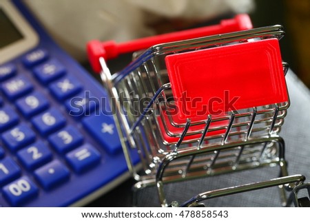 Miniature model of shopping cart trolley put on dark background in the scene appear calculator as a background represent the shopping and retail business background concept related idea.