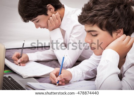 Two teenage boys doing homework at home, writing something in their notebooks, enjoying studies, education concept