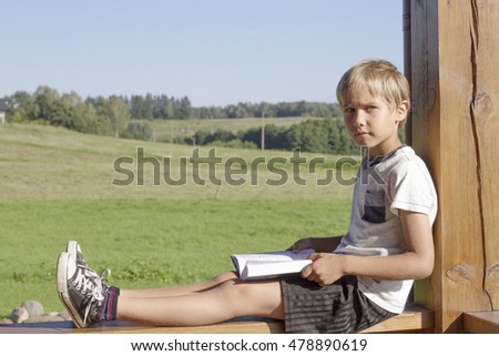 Little boy reading book at summer terrace. Casual clothes. Nature background. People, education, knowledge concept