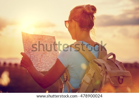 Rear view of a traveler girl with backpack exploring map, enjoying mild sunset light, active people lifestyle, summer fun vacation, traveling around the world  Royalty-Free Stock Photo #478900024