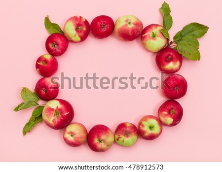 Top view on delicious red organic apples with leaves in a shape of circle on light pink background. Healthy food concept
