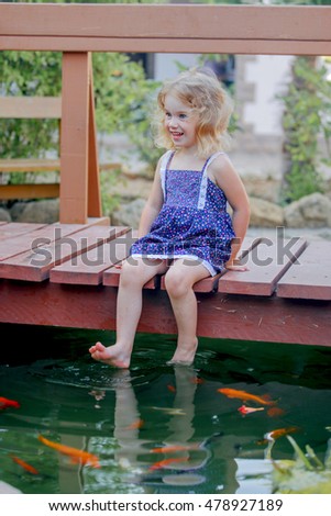 Curly kid girl playing with fishes in a pond