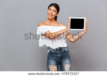 Beautiful young woman showing tablet computer with blank screen isolated on a gray background